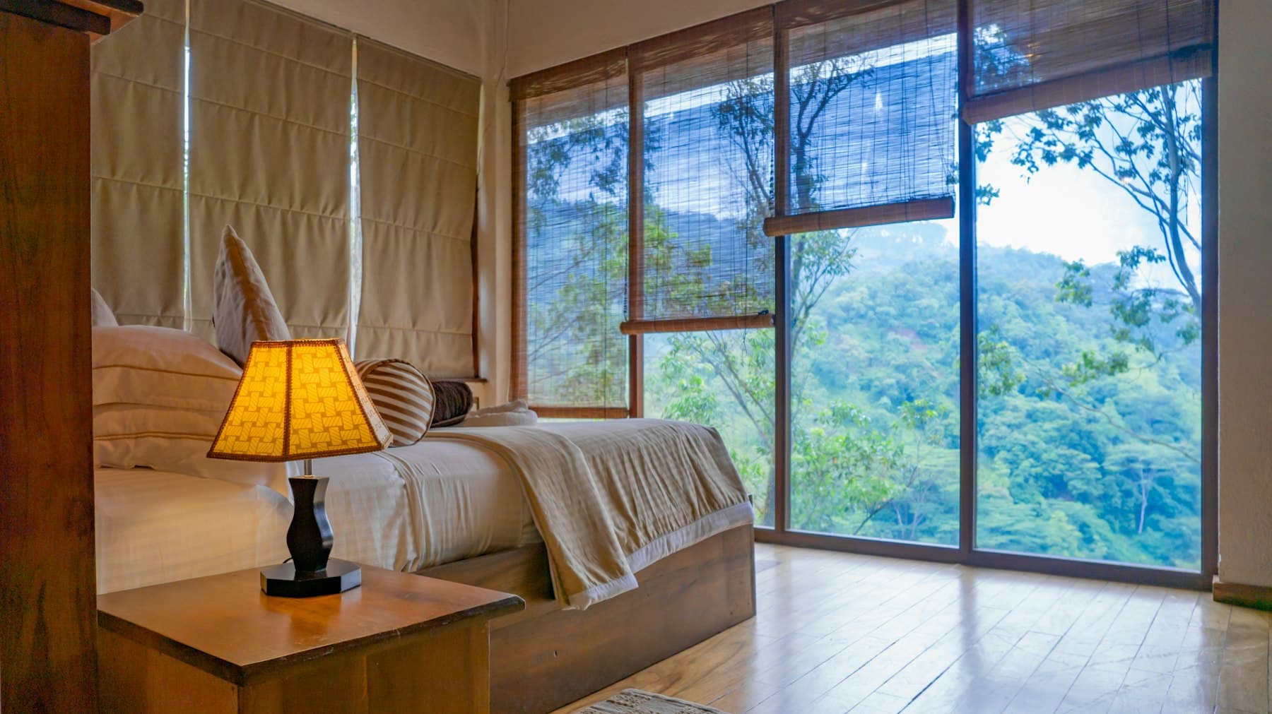 A double bed in front of a glass wall looking onto the garden trees