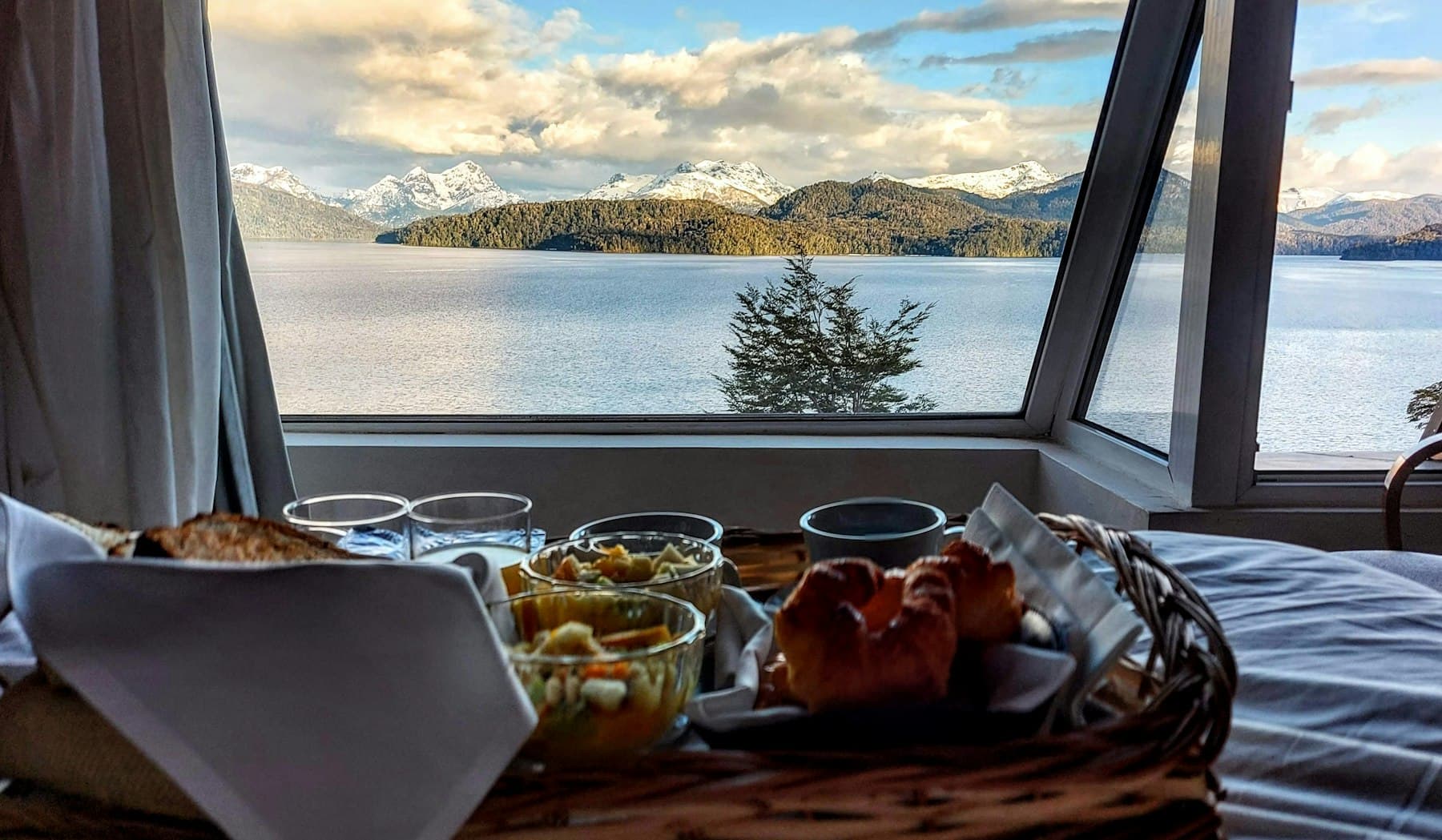 A breakfast tray on the bed, in front of the window over the lake